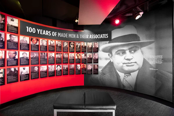Een tentoonstelling in het museum met een grote foto van een man met hoed en pak, getiteld "Made Men & Their Associates", met kleinere afbeeldingen en tekst.