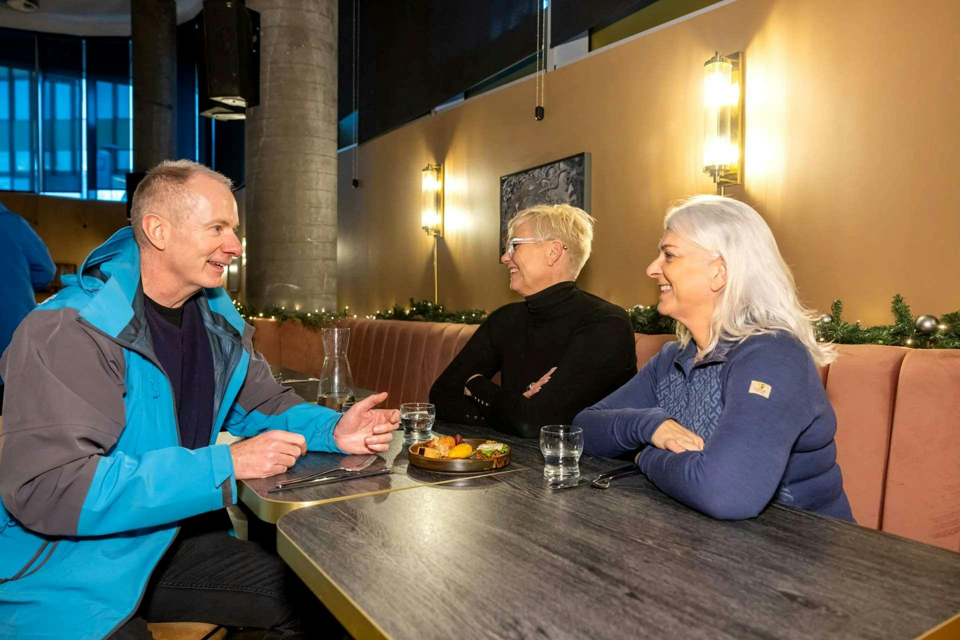 Two people conversing at a restaurant table, with plates of food and glasses of water in front of them.