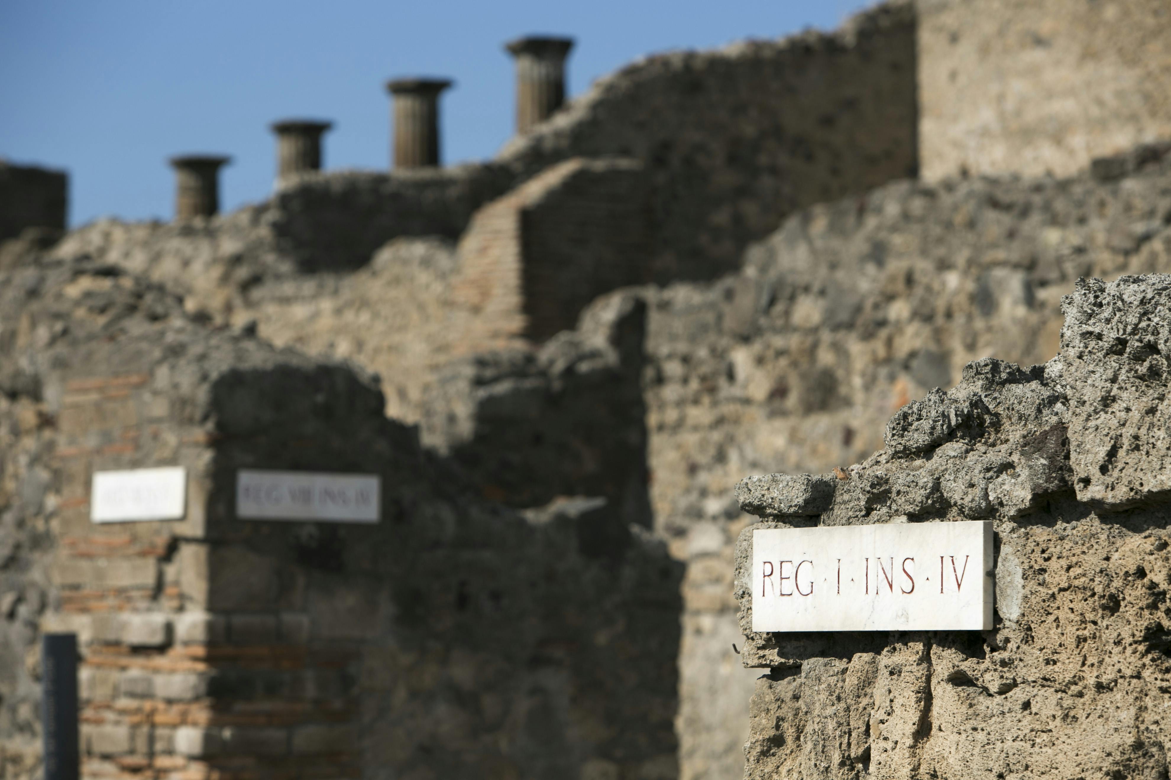 古老的石头遗迹上有拉丁文铭文，晴朗的蓝天下有多个石柱和墙壁。