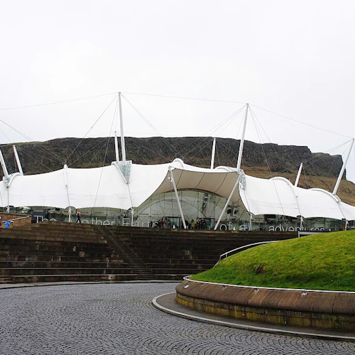 Modern byggnad med stort vitt krontak, belägen på en kulle med kullerstensväg och stentrappor som leder till ingången.
