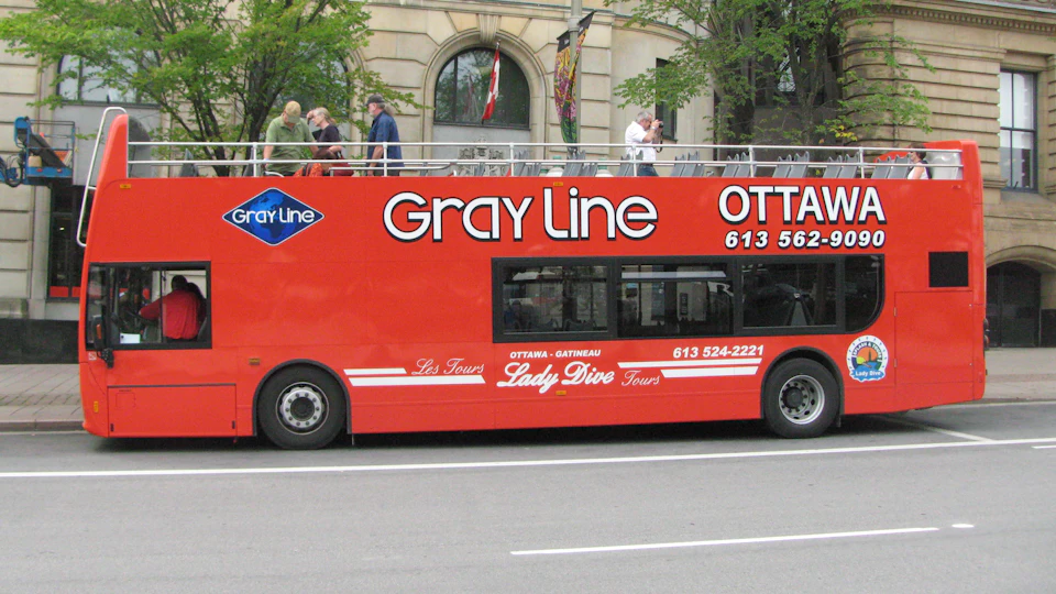 A red Gray Line double-decker tour bus with people on the upper level, parked on a city street.
