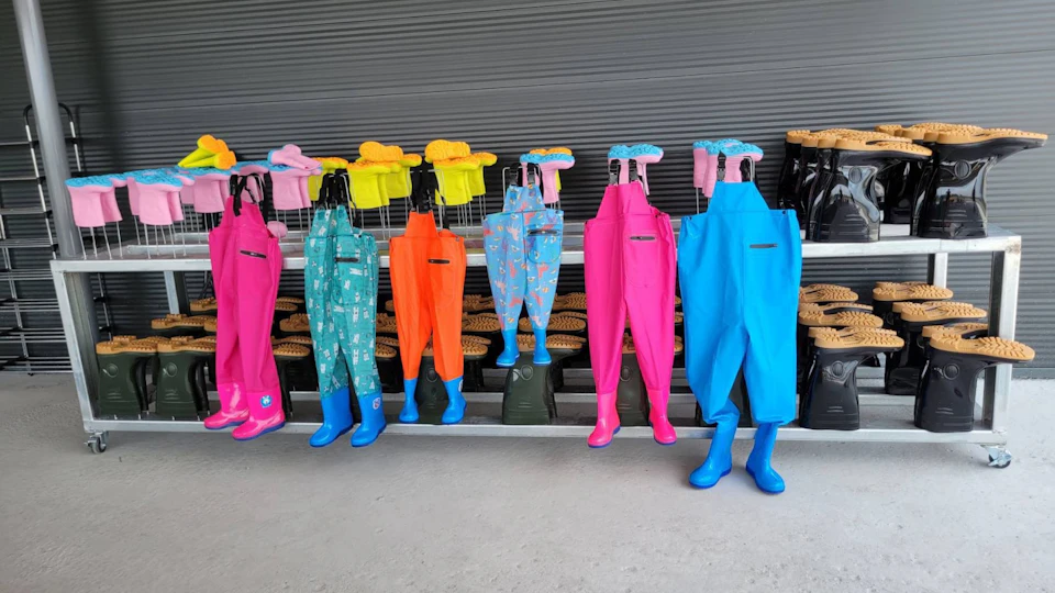 Colorful children's rain gear, including waders and boots, displayed on mannequins in front of a gray background.
