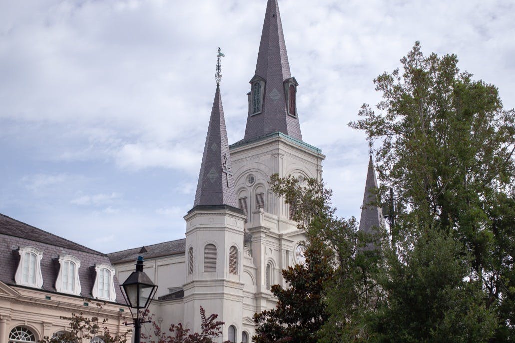 Γοτθικού ρυθμού καθεδρικός ναός με τρεις πυργίσκους, ορατό φύλλωμα και μια λάμπα δρόμου σε πρώτο πλάνο με φόντο έναν συννεφιασμένο ουρανό.