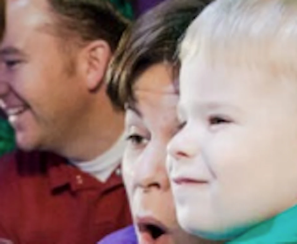 A young boy points excitedly at stingrays and fish in an aquarium tank, while a woman kneels beside him and others look on.
