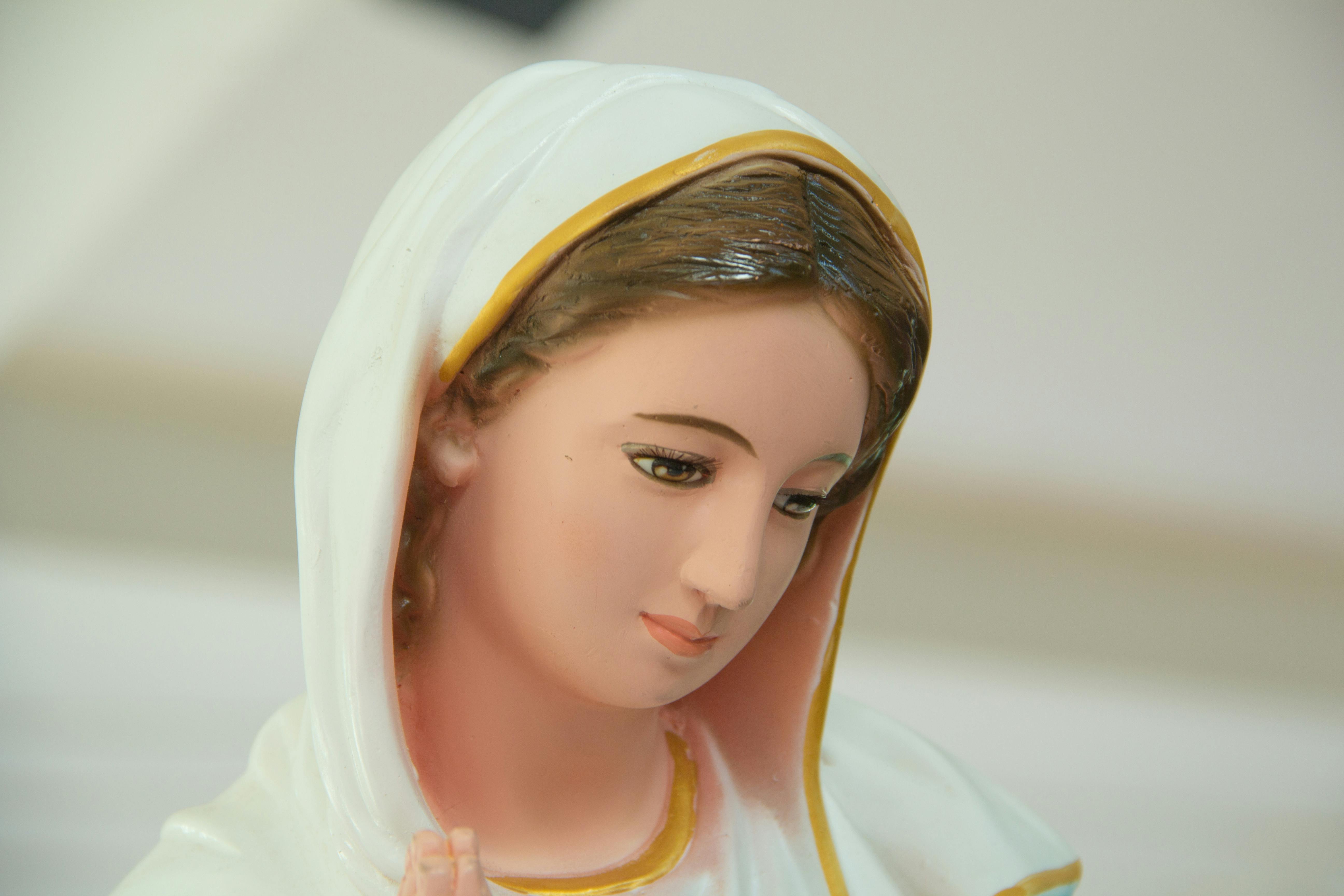 Close-up of a statue of a serene-faced woman with a white and gold-trimmed head covering, looking downward.