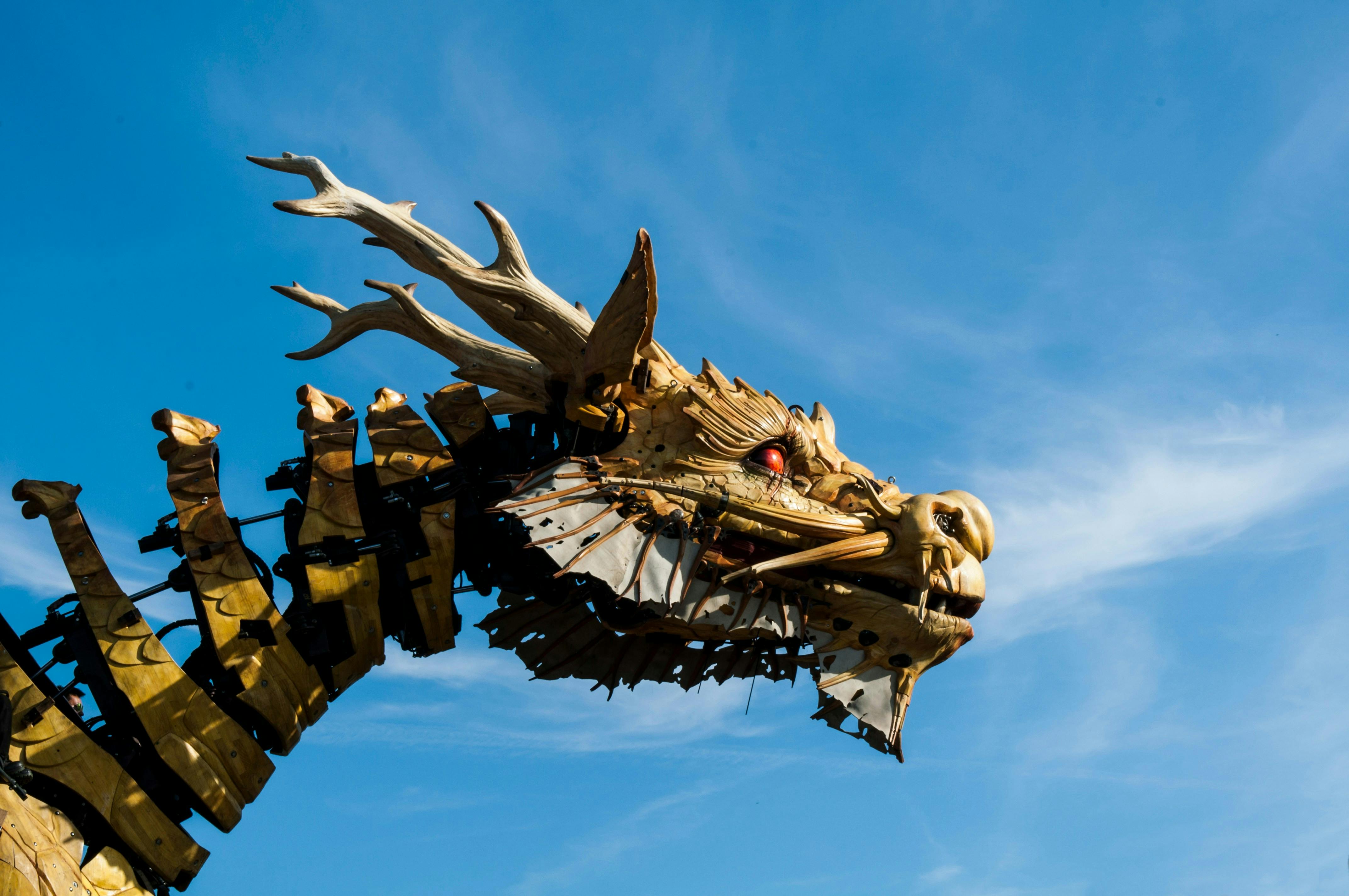 Wooden dragon sculpture with intricate details and mechanical parts against a clear blue sky.