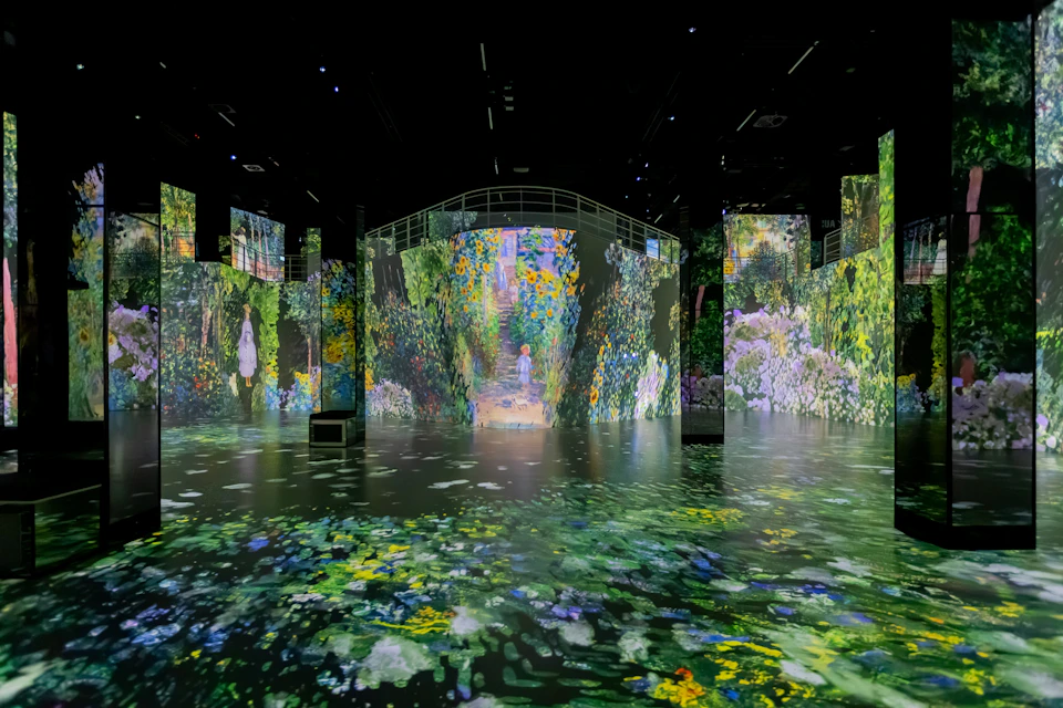 Immersive digital installation of a garden with vibrant floral projections on walls and floors in a dark room.