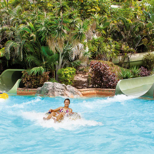 Menschen, die Wasserrutschen in einem von üppigem Grün und tropischen Pflanzen umgebenen Pool genießen.