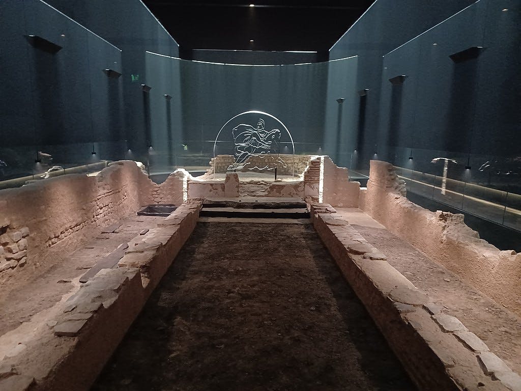 Expozice muzea zobrazuje starobylé kamenné zříceniny v temné místnosti s osvětlenou rytinou koně a jezdce na konci.