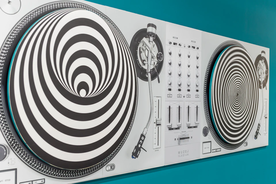 A wall-mounted art piece resembling a DJ turntable setup with hypnotic black-and-white spiral patterns on the vinyl discs.