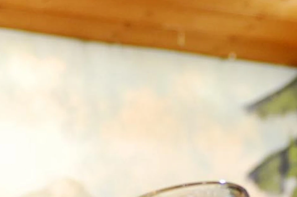 A woman wearing traditional attire holds a large glass mug of beer, smiling, with a painted countryside backdrop behind her.