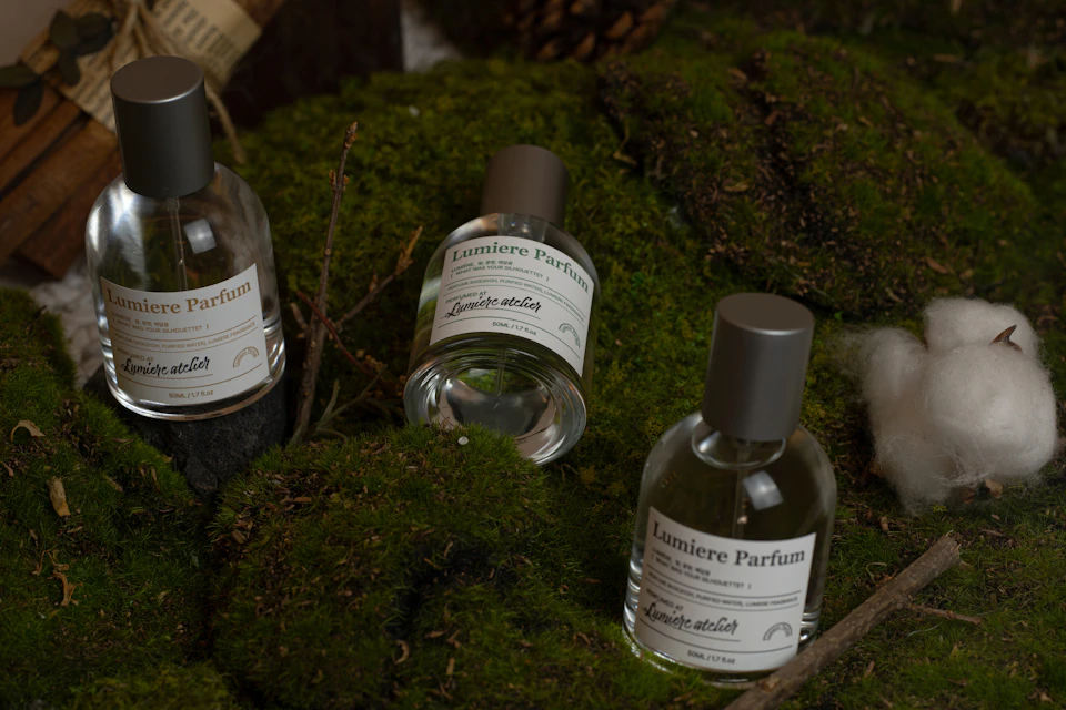 Three glass bottles of perfume labeled 'Lumiere Parfum' displayed on a bed of green moss with natural elements.
