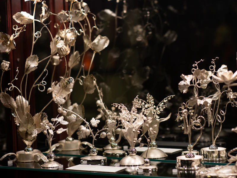 Esculturas de flores metálicas intrincadamente elaboradas sobre una superficie reflectante, con un fondo oscuro y difuminado.
