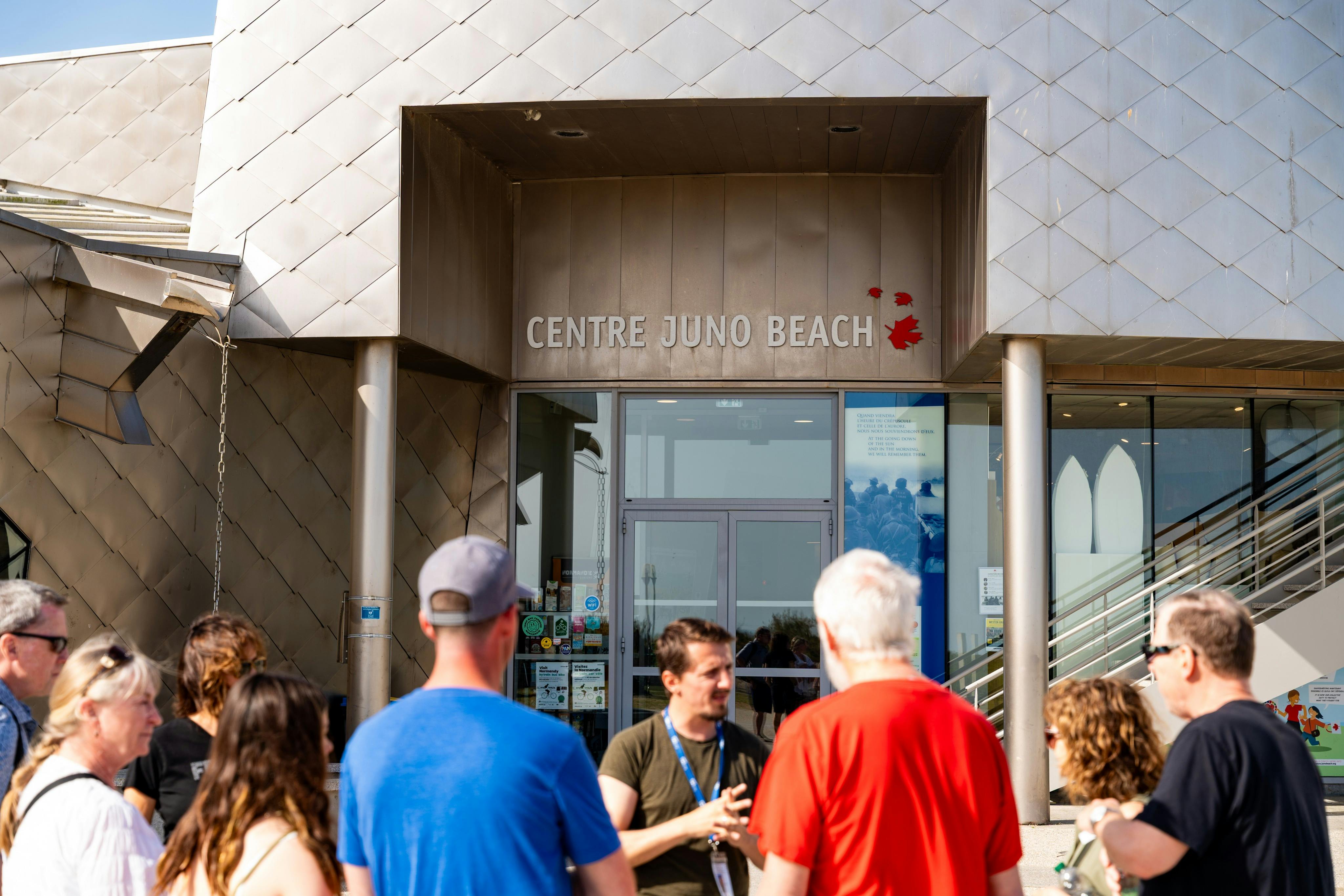 A group of people standing in front of the Centre Juno Beach entrance, with the building's name and logo visible above.