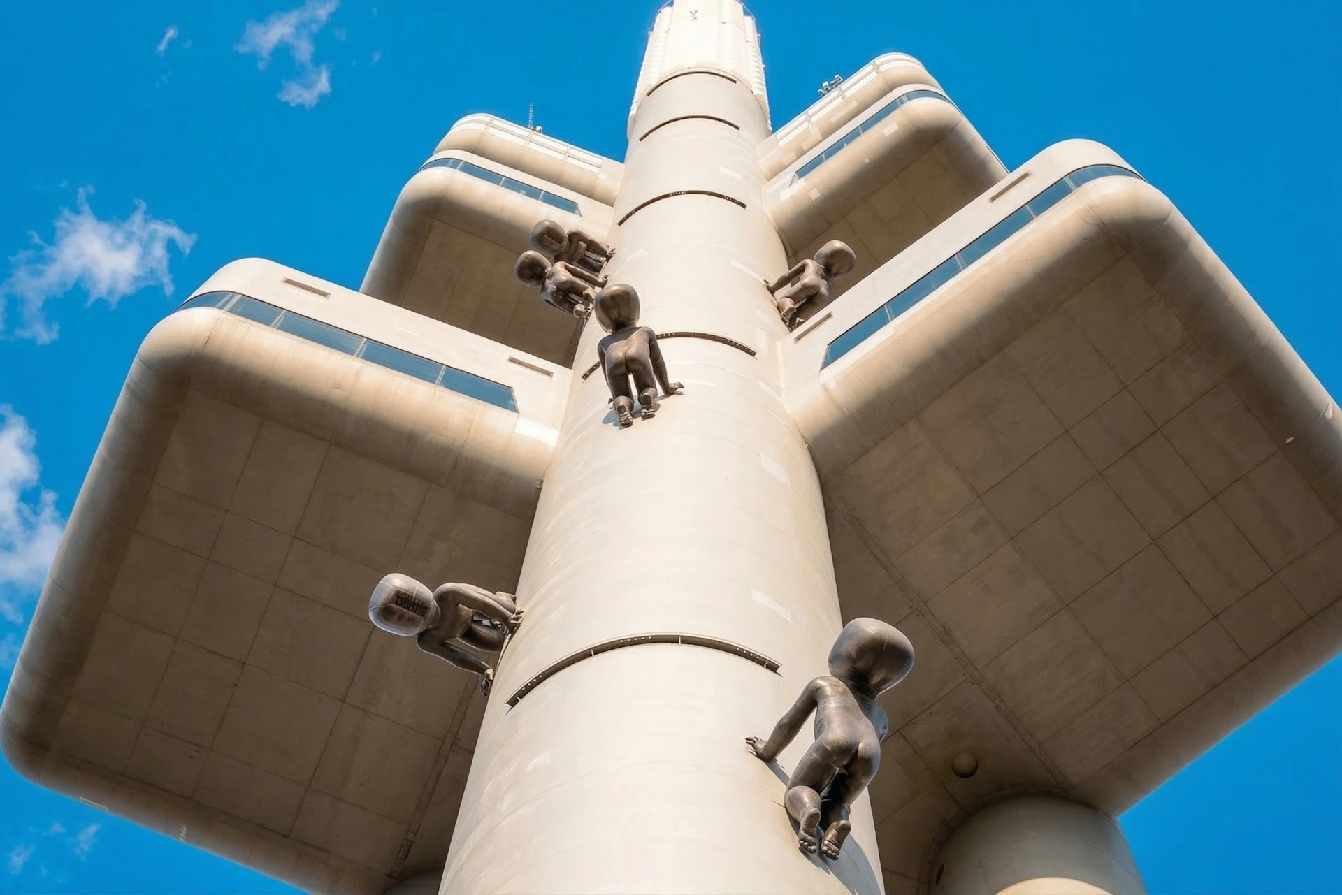 A tall concrete tower with large protruding platforms, featuring statues resembling crawling babies on its surface.
