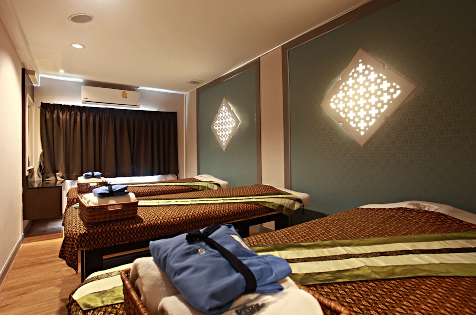 A spa room with three massage beds, decorative wall lights, and neatly folded towels and robes on baskets.