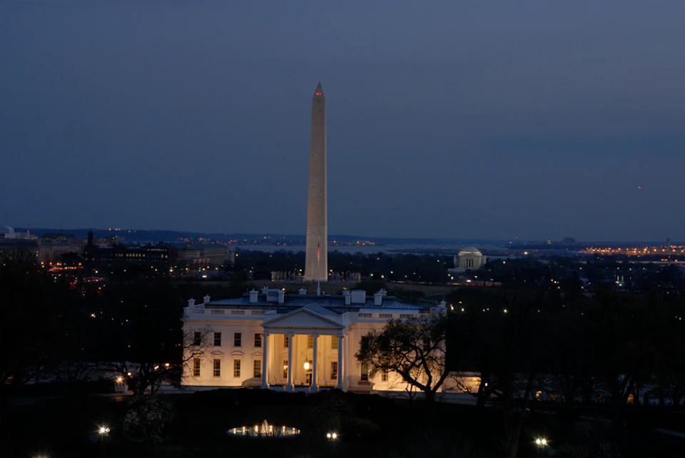 The White House illuminated at dusk with the Washington Monument and Jefferson Memorial visible in the background.