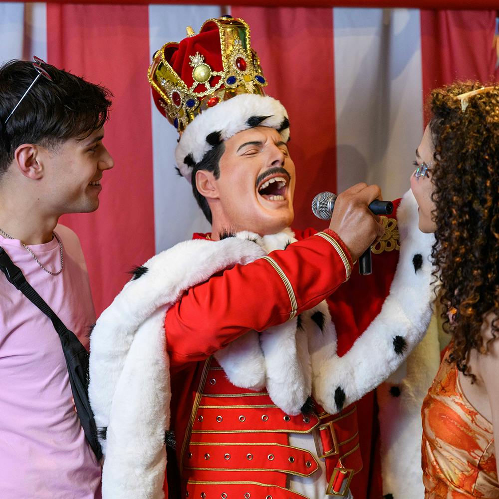 A statue dressed as a king holds a microphone to the face of a smiling woman, with a man standing next to her.