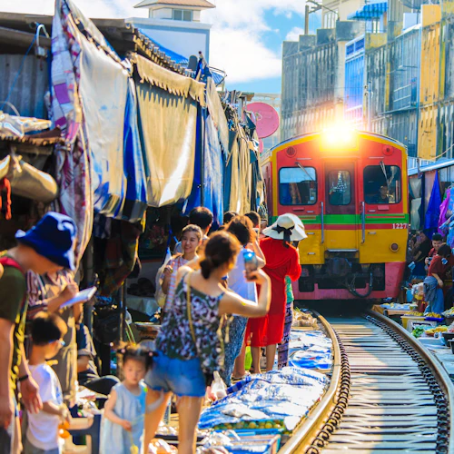 Ein Zug fährt durch einen belebten Markt, mit Ständen und Menschen auf beiden Seiten, die fotografieren und einkaufen.