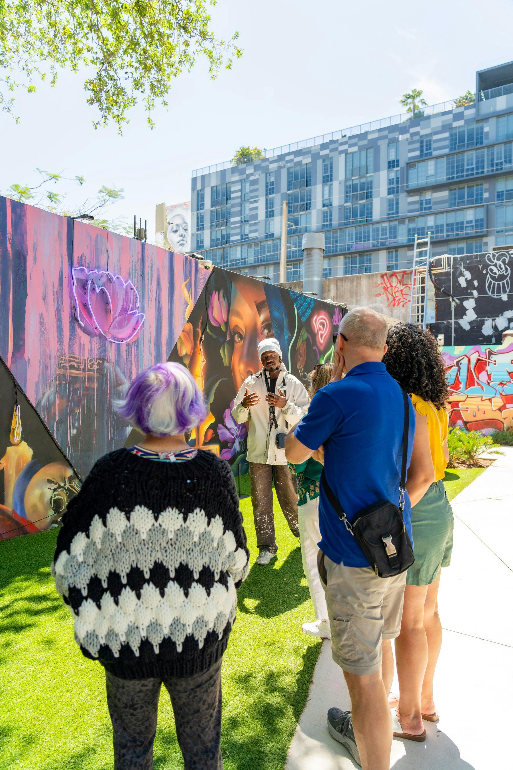 一群人观察并聆听艺术家在户外城市画廊空间中解释色彩缤纷的壁画。