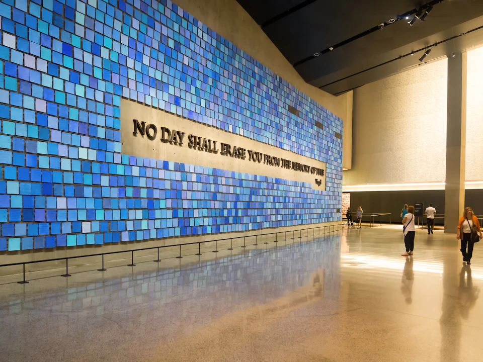 A large mosaic of blue tiles with the text "No Day Shall Erase You From the Memory of Time." Two people observe from a distance.