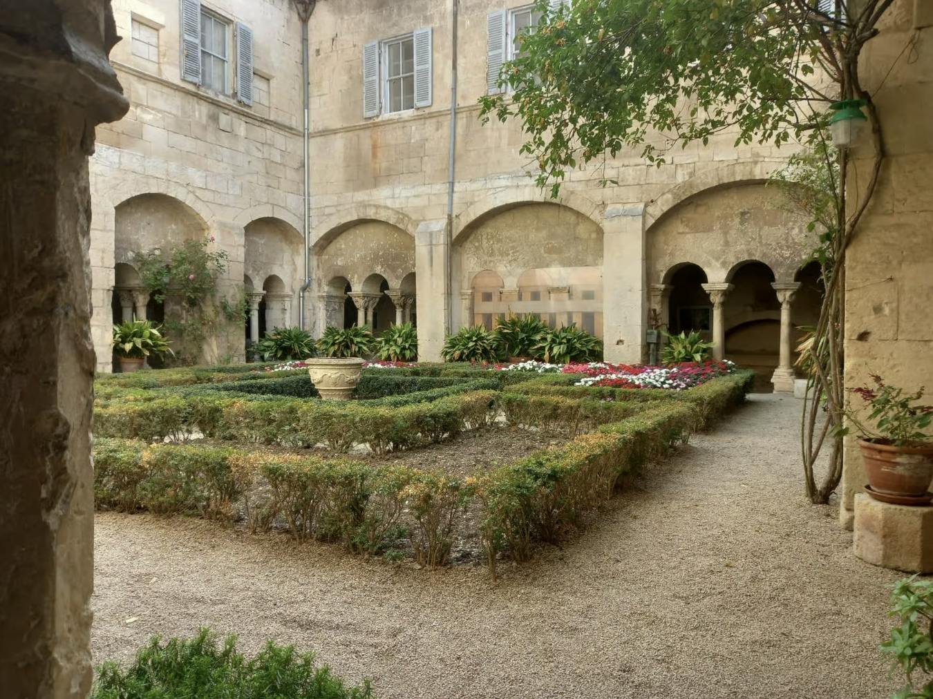 一座历史悠久的建筑的封闭式庭院，有拱形柱廊、修剪整齐的树篱、花坛和中央石头种植园。