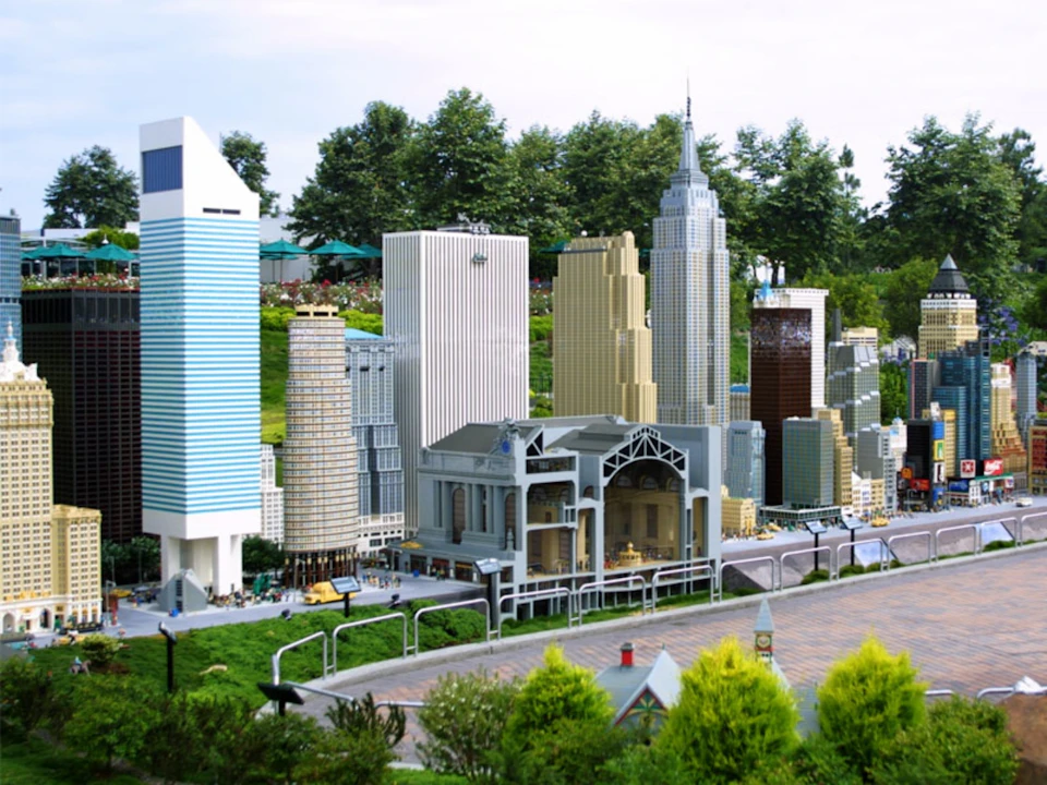 Miniature cityscape with various high-rise buildings, a prominent structure resembling a train station, and trees in the background.