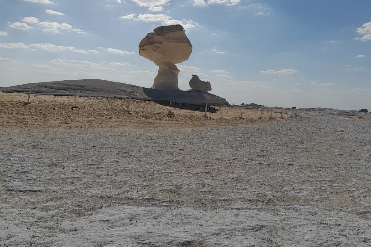 A large mushroom-shaped rock formation in a desert landscape under a partly cloudy sky.