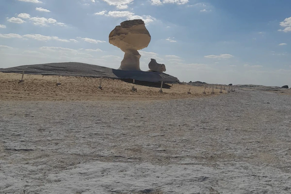 A large mushroom-shaped rock formation in a desert landscape under a partly cloudy sky.