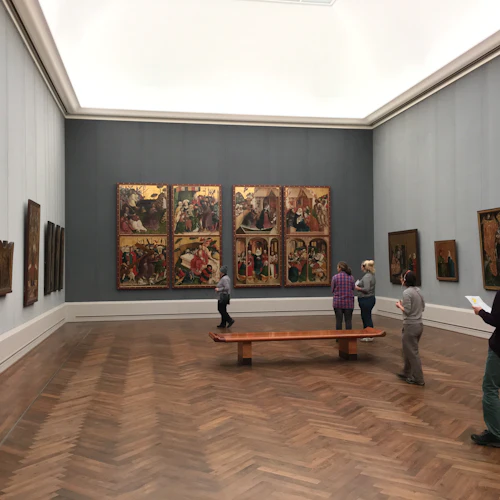 Ett museigalleri med flera personer som tittar på målningar på väggarna och en träbänk i mitten av rummet.