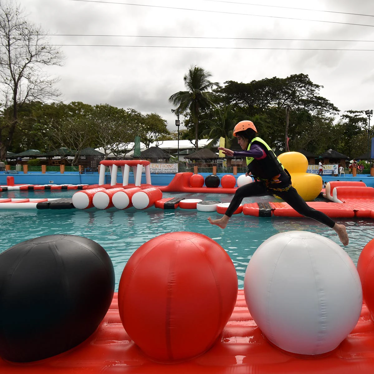 A person wearing a helmet and life jacket jumps across large inflatable balls on a water obstacle course.