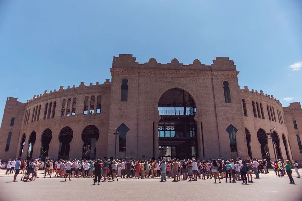 A large crowd gathers in front of a historical brick building under a clear blue sky.