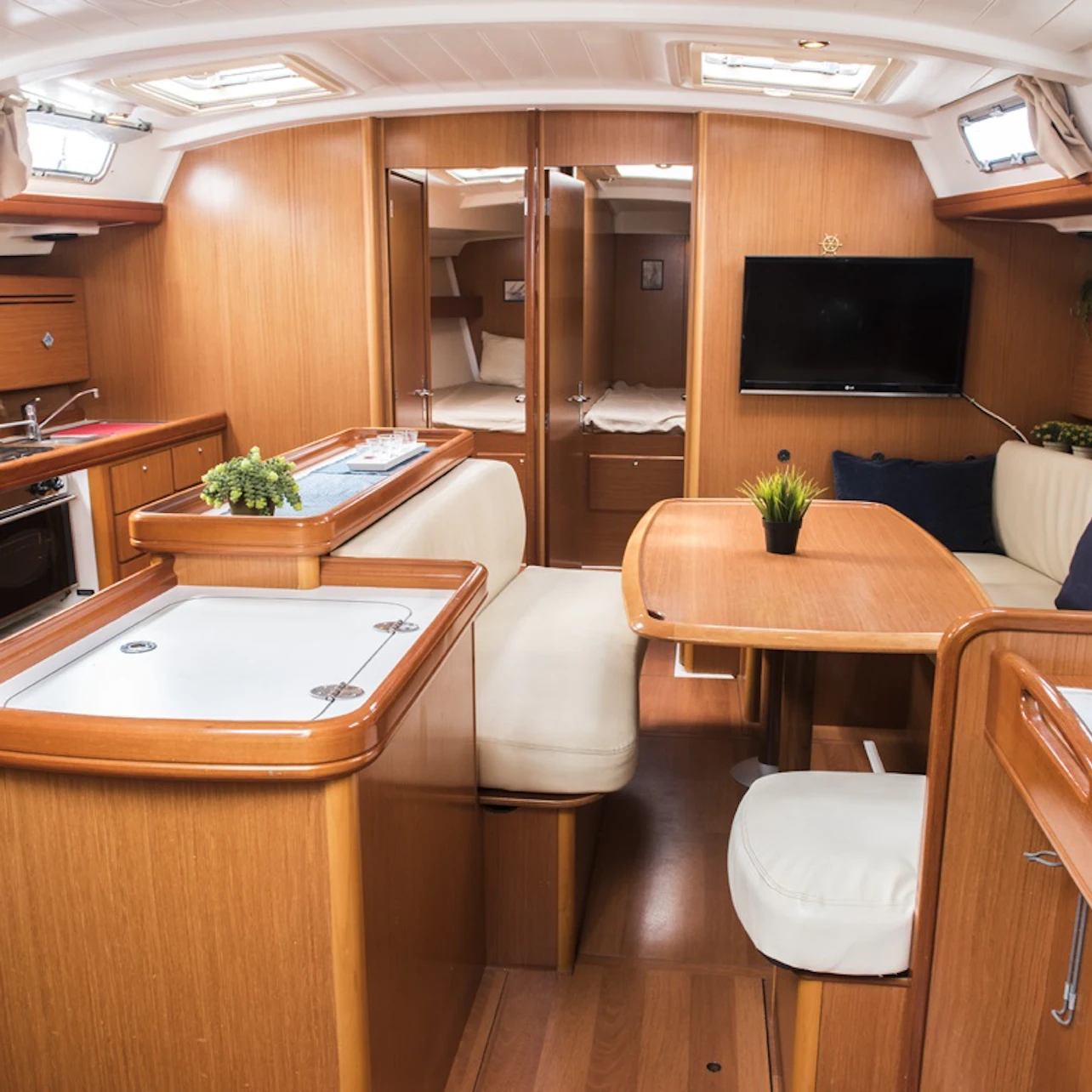 A neatly organized boat interior with a kitchen area, seating, a table with plants, and a television mounted on the wall.