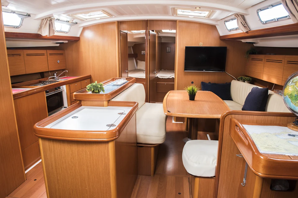 A neatly organized boat interior with a kitchen area, seating, a table with plants, and a television mounted on the wall.
