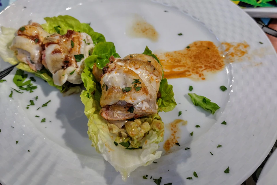 Chicken pieces on lettuce leaves, garnished with herbs and sauce, served on a white plate.