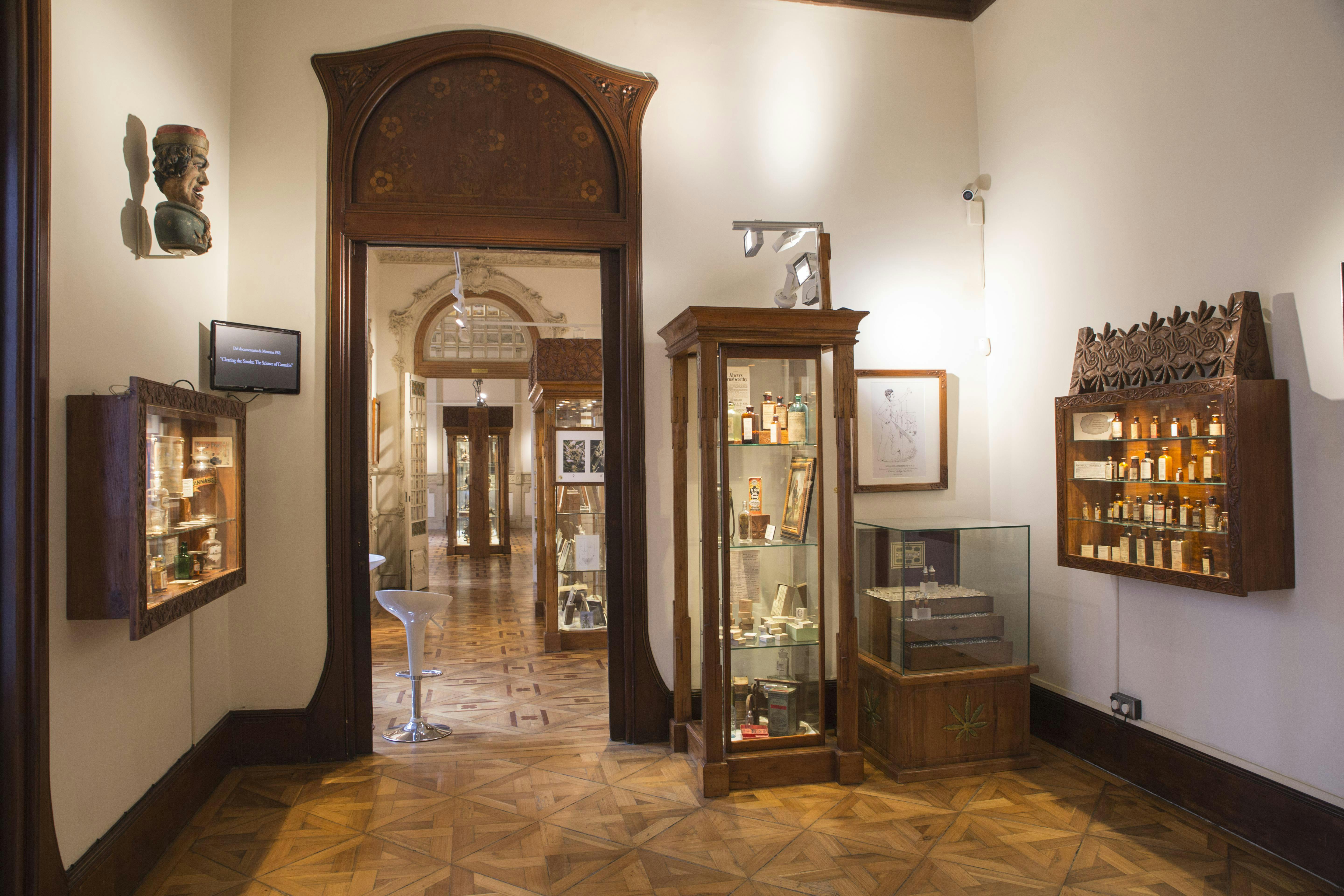 An ornate room in a museum with display cases, a bust, and wooden flooring. A doorway leads to a well-lit corridor.