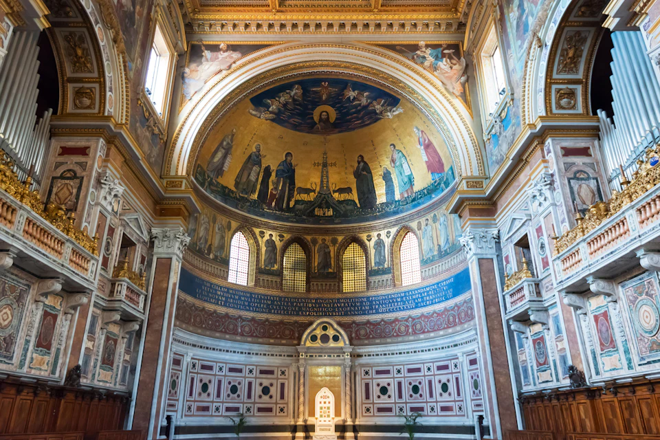 A richly decorated church interior with a gold mosaic dome depicting religious figures and scenes, illuminated by natural light.