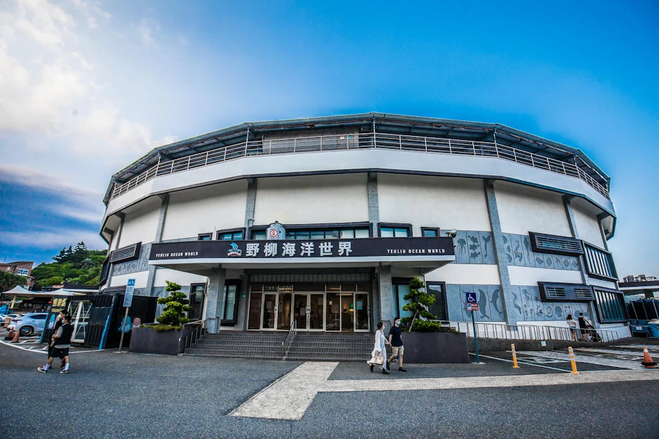 A building labeled 'Yukai Ocean World' with people walking in front, featuring a curved facade and clear blue sky above.