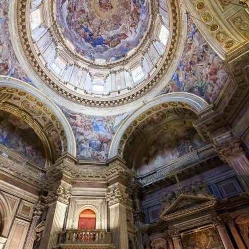 Ornate cathedral interior with detailed frescoes on domed ceilings and archways, showcasing religious scenes and figures.