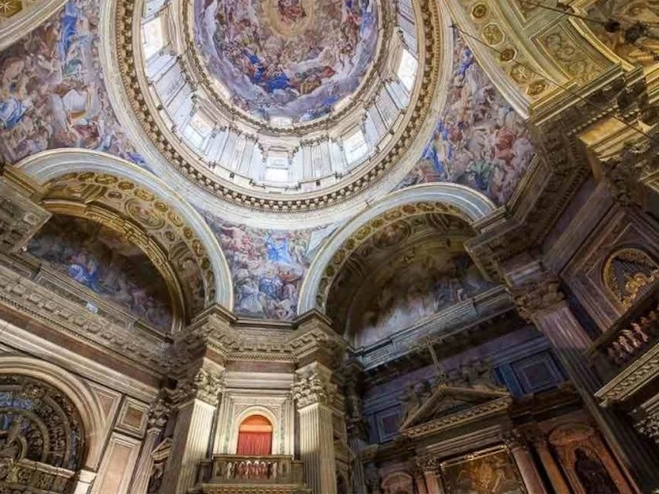 Ornate cathedral interior with detailed frescoes on domed ceilings and archways, showcasing religious scenes and figures.