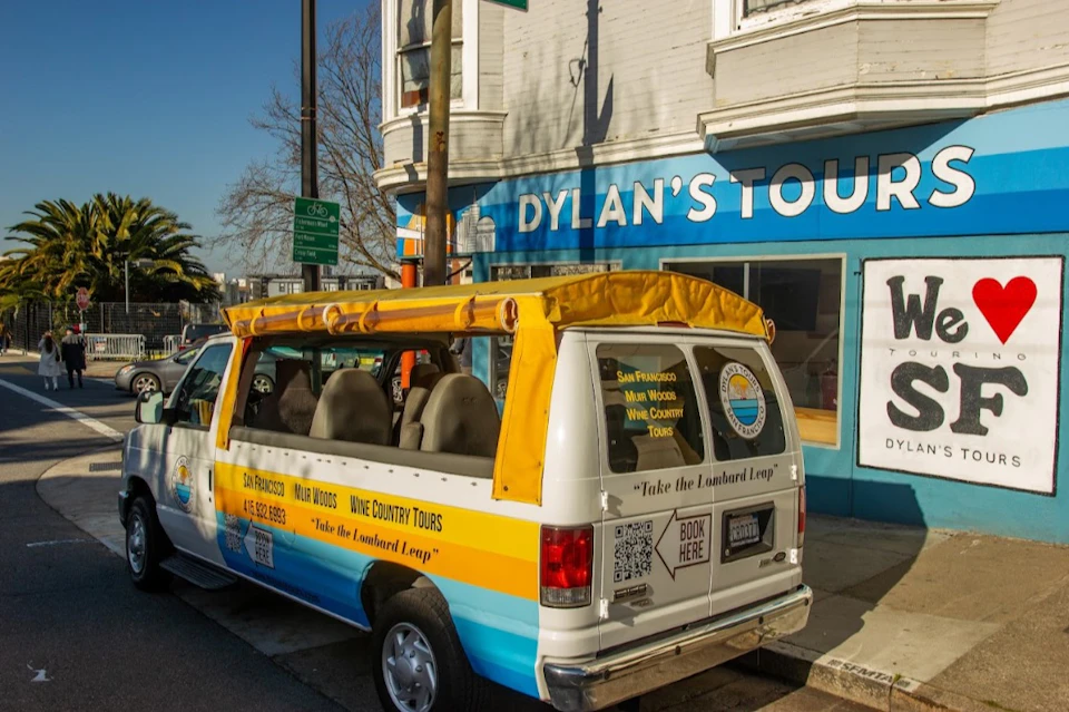 A van with a yellow canopy parked in front of a tour office with a sign that reads "Dylan's Tours."