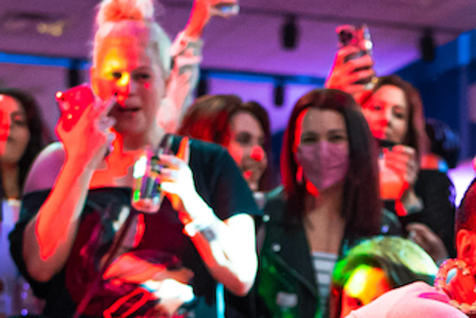 Person dancing energetically with a cloth in their hand, surrounded by a crowd taking photos and reacting enthusiastically.