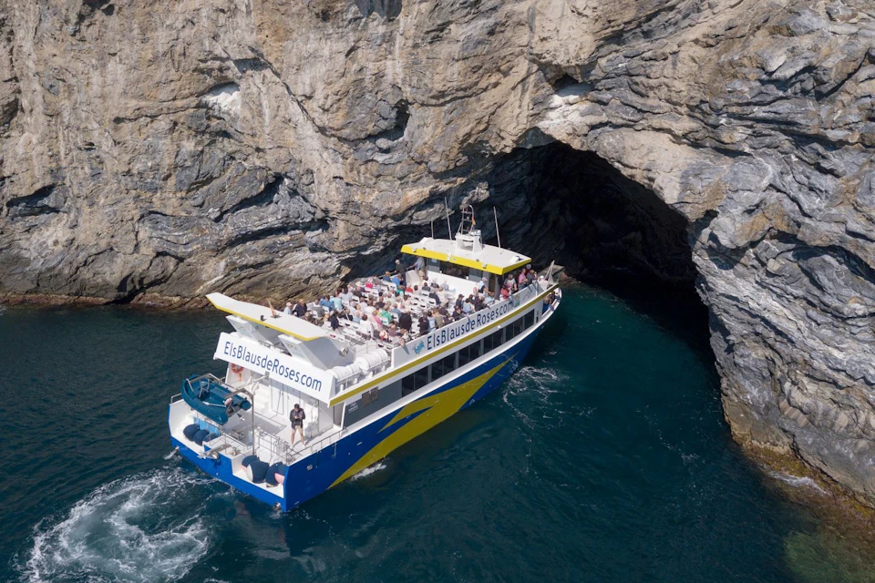 A boat with passengers approaches a rock cavern on a coastline, with 'ElsBlausdeRoses.com' visible on its side.