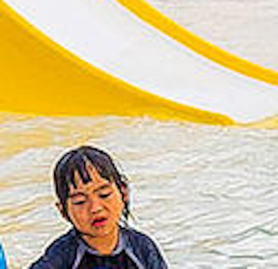 Children playing on a splash pad with colorful water features, including slides and spraying structures, on a bright day.
