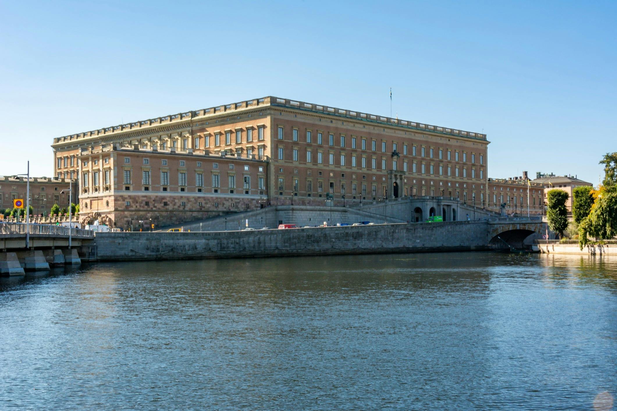 Large rectangular building with many windows, situated next to a river under a clear blue sky.