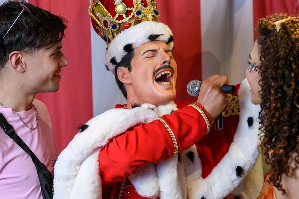 Socha oblečená jako král drží mikrofon u tváře usmívající se ženy a vedle ní stojí muž.