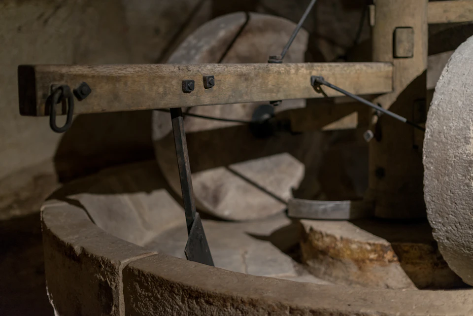 Close-up of a rustic, old-fashioned millstone grinder with wooden and metal components in low light, showcasing weathered textures.