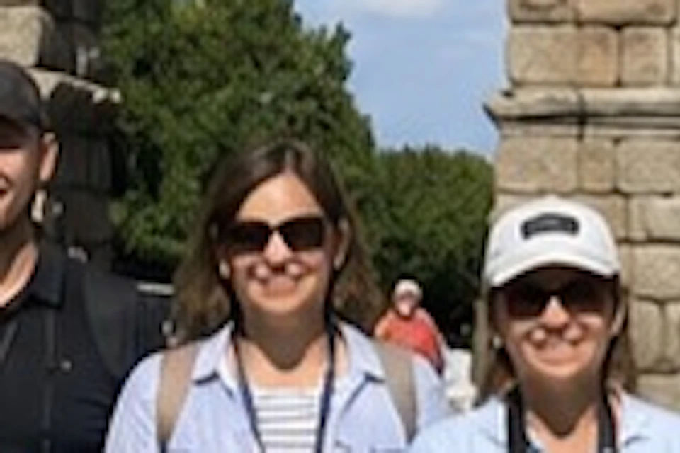 A group of people posing in front of an ancient stone aqueduct on a sunny day.
