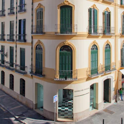 Corner of a beige building with green shuttered windows, arched doorways at street level, and ornate architectural details.