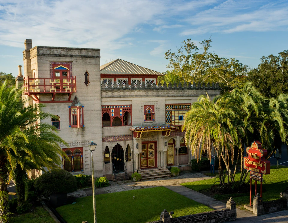 A two-story, ornate building with colorful windows and doorways surrounded by palm trees and greenery under a blue sky.